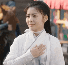 a woman in a white kimono with her hand on her heart
