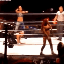 a woman is standing in a wrestling ring with a referee watching .