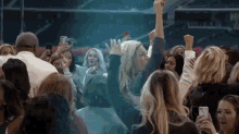 a crowd of people are dancing in a stadium while holding their phones .
