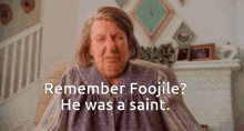 an elderly woman is sitting in front of a fireplace with the words remember foojile he was a saint