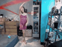 a woman in a pink dress is dancing in a room with a scale on the floor