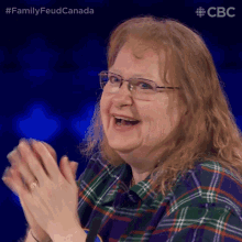 a woman wearing glasses and a plaid shirt applauds in front of a cbc logo