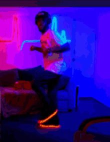 a man is dancing in a living room with neon lights behind him