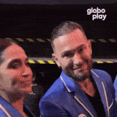 a man in a blue suit is smiling next to a woman in a black shirt with the word globo play on the bottom right