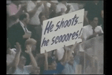a crowd of people holding up a sign that says he shoots he scooores .