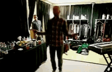 a man in a plaid shirt is standing in a room with clothes on a rack