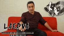 a man sits on a red couch in front of a sign that says laedva on it
