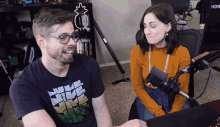 a man and a woman are sitting in front of a microphone and the man is wearing a purple nike shirt