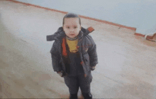 a young boy in a jacket and overalls is standing in a room .