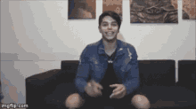 a man in a blue jacket is sitting on a couch and smiling .