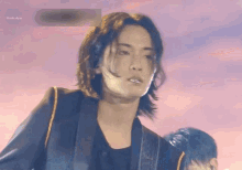 a young man with long hair is playing a guitar on stage .