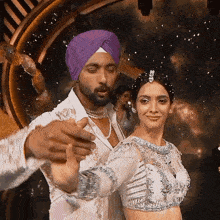 a man wearing a purple turban is dancing with a woman