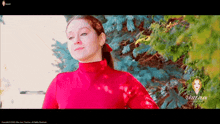 a woman in a red turtleneck is standing in front of a pine tree