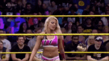 a woman in a pink top is standing in a wrestling ring with a crowd watching .