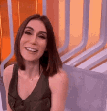 a woman is smiling and sitting on a couch in front of a wall .