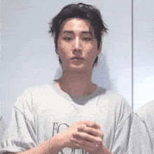 a young man wearing a gray t-shirt is holding his hands together .