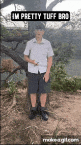 a boy in a white shirt and black shorts stands next to a tree