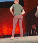 a man in a green shirt and pink pants stands on a stage with his hands in his pockets