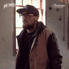 a man wearing glasses and a hat stands in front of a paramount network sign