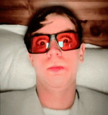 a man wearing red sunglasses is laying on a pillow