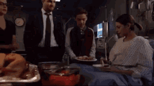 a group of people are standing around a woman sitting in a hospital bed .