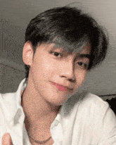 a young man wearing a white shirt and a chain around his neck is smiling