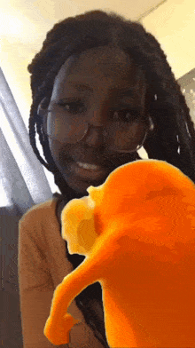 a woman with dreadlocks and glasses is smiling and looking at an orange object in front of her