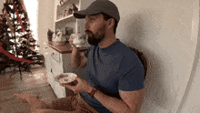 a man with a beard is sitting in front of a christmas tree holding a plate of food