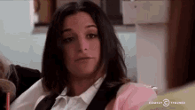 a woman in a white shirt and pink sweater is sitting in a chair and making a funny face .