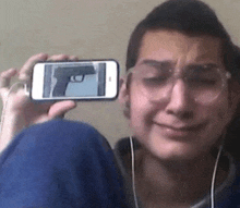a man is crying while holding up a cell phone with a gun on it