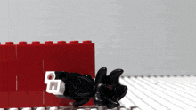 a black lego figure is laying on a table next to a red brick