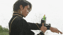 a man in a black and gold outfit is holding a green bottle on his wrist