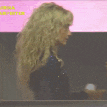 a woman with blonde curly hair is standing in front of a screen that says sabrina carpenter on it