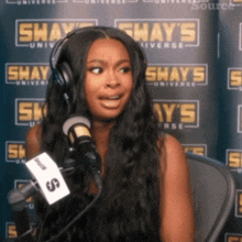 a woman wearing headphones and a microphone in front of a shay 's universe banner