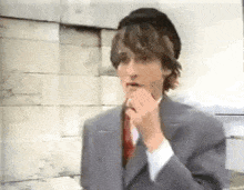 a man in a suit and tie is holding his hand to his mouth and looking at something .