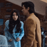 a woman in a blue coat is standing next to a man in a brown suit with divahyunju written on the bottom right