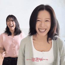 a woman in a white tank top smiles while another woman in a pink cardigan laughs behind her