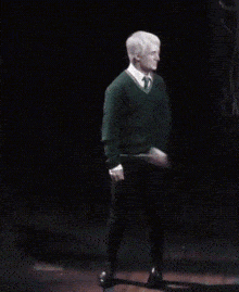 a man in a green sweater and tie is dancing on a stage in the dark .