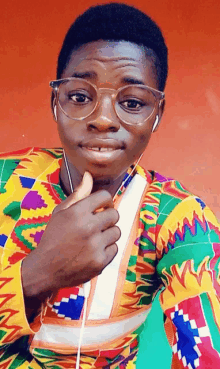 a young man wearing glasses and a colorful shirt has a thumb up