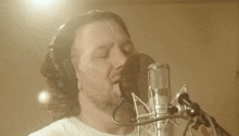 a man wearing headphones is singing into a microphone with his eyes closed