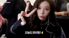 a woman is making a peace sign with her fingers while wearing a black jacket .