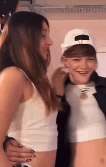 two girls are standing next to each other in a room . one of the girls is wearing a white hat .
