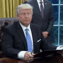 a man in a suit and tie is sitting at a desk with his eyes closed and a pen in his hand .