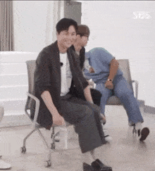 a man in a suit is sitting in a chair with his legs crossed while two other men sit in chairs .