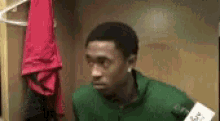 a man in a green shirt is standing in a locker room with a microphone in his hand .