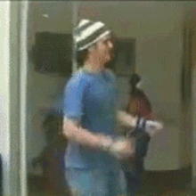 a man in a blue shirt and striped hat is standing in a room