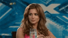 a woman is sitting at a table with a glass of water and a pen in front of a sign that says fox 21