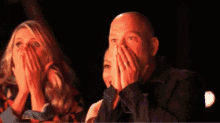 a man and a woman are covering their faces with their hands .