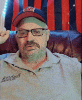 a man wearing a hat and glasses is sitting in front of a red and blue striped curtain