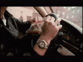 a man wearing a watch is driving a car and opening a bag